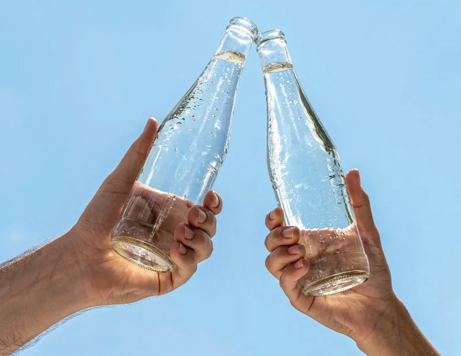 Dos personas brindando con botellas de vidrio
