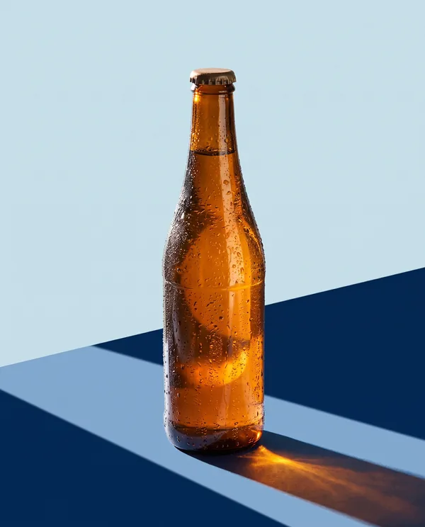 Botella de cerveza ámbar con condensación sobre dos planos de color, azul cielo y azul marino